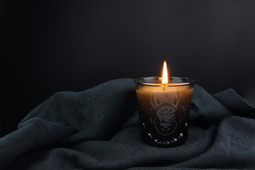 the burning luxury aromatic scent candle glass is on the black table decorated with black cloth in...