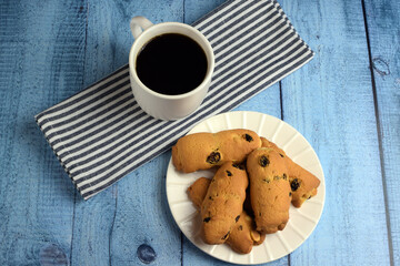 White cup with on a kitchen cotton napkin, homemade raisin cookies on a colored wooden table. The concept of home breakfast, afternoon tea. Tea ceremony. Side and top view.