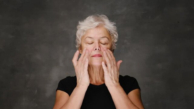 Portrait of Beautiful Senior Woman gently Applying Under Eye Face Cream. Elderly Lady Makes Her Skin Soft, Wrinkle Free with Natural anti-aging Cosmetics