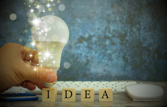 Hand stroking a light bulb on a wood block with Word Ideas, fresh idea concept with innovation and inspiration, revolutionary science and communication concept