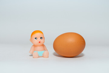 Miniature newborn baby toy and egg sitting on a white gray background.Selective focus,copy space.