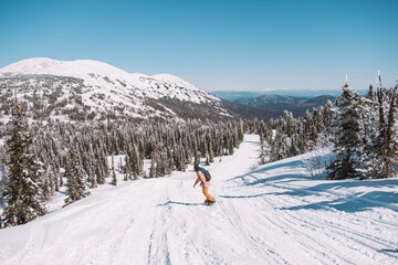 Russia. Sheregesh. Girl snowboarder in sun goggles in winter in sunny weather outdoors among the mountains and snow. Spring. Girl rides a snowboard in the distance, silhouette of a man among nature