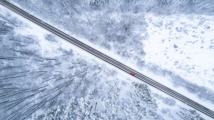 Aerial top down drone shot of Snowy forest road with red car on it. Forest road from above