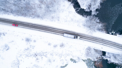 Aerial top down drone shot of Snowy road with red car and white truck on it. Forest road from above