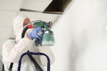 Male worker painting wall with spray gun in white colour, busy handyman at work