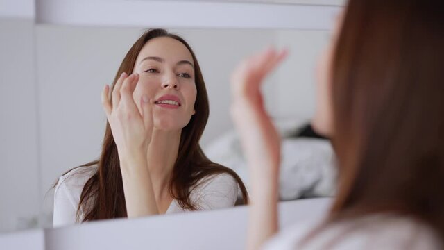 Glad female applying concealer and smiling
