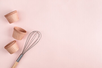 The concept of homemade baking is a whisk for whipping and cupcake molds on a pink background. zero waste. Copy space.