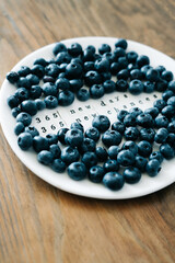 a white plate with a motivational phrase and fresh ripe blueberries on a wooden table