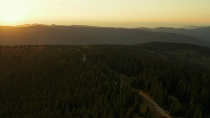 Aerial mountain sunrise view against golden morning sky green trees road scene