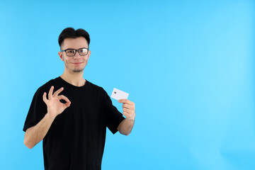 Fototapeta premium Attractive guy with credit card on blue background