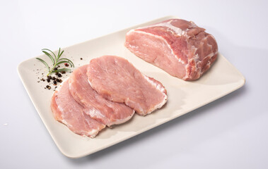 Fresh raw meat, pork loin in cross-section and sliced in chops on a white plate, isolated on white....