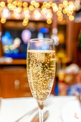A glass of champagne on the festive table against the background of congratulations on TV on New Year's Eve
