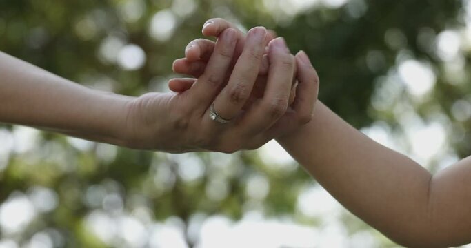 4K Video slow motion mom and daughter holding hand with green park background. Concept of family connection of mother and kids.