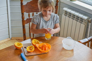 the child girl in the kitchen cuts and squeezes oranges juice