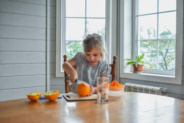 the child girl in the kitchen cuts and squeezes oranges juice
