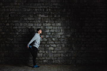 Obraz na płótnie Canvas Hispanic teenager sportsman stretching against wall in the darkness.