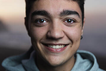 Closeup portrait of hispanic teenager boy smiling and looking to the camera at sunset