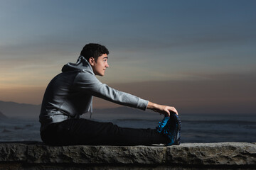 Hispanic teenager stretching hamstring muscles at sunset.