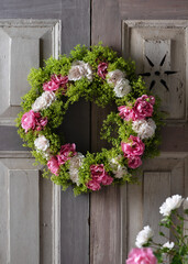 Beautiful summer flower wreath made of pink and white roses and lady's mantle blossom hangs on old weathered wooden door. Garden or home decorations concept. Selective focus. © Oksana Schmidt