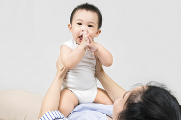 Motherhood Concept - Smiling young woman holding baby boy while lying on back, embracing Her Cute Infant Son, Loving Mom Enjoying Time With Her Baby.