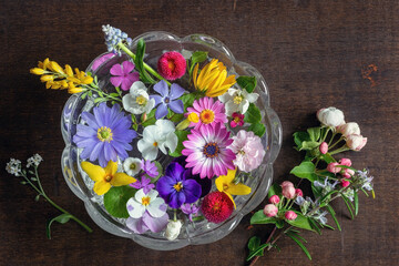Fototapeta na wymiar Runde Glasschale mit bunten schönen Blüten steht auf alten Holztisch im Frühling