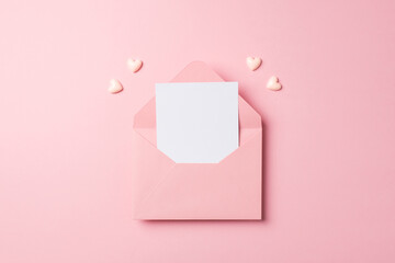 Top view photo of valentine's day decorations open pink envelope with paper sheet and pink hearts on isolated pastel pink background with empty space