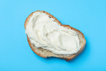 Slice of bread with tasty cream cheese on light blue background, top view