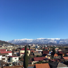 Naklejka na ściany i meble Landscape. The roofs of houses against the blue sky and snowy mountains on the horizon.