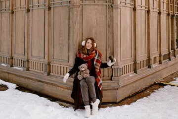 Young woman in winter clothes and fur earmuffs. Girl with teddy bear and mulled wine