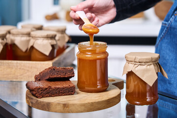 Fototapeta na wymiar a woman's hand holds a spoon on which homemade caramel flows into a jar