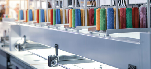 Colorful rows spools of thread stand on embroidery machine in garment industry.