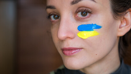 Indoor portrait of young girl with blue and yellow ukrainian flag on her cheek wearing military uniform, mandatory conscription in Ukraine, equality concepts