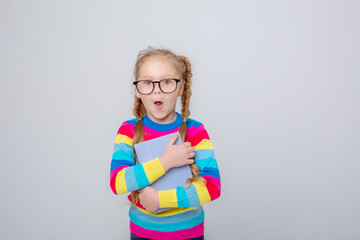 a cute little girl in a multicolored sweater and glasses holds a book on a white background , smiling
