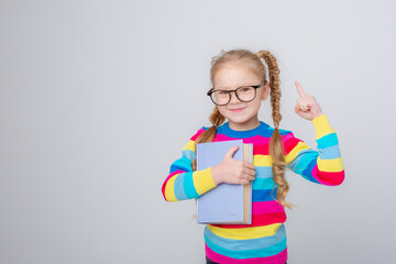 a cute little girl in a multicolored sweater and glasses holds a book on a white background , smiling