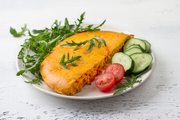 Vegan chickpea omelet with bell peppers served with tomatoes, cucumbers, lettuce and parsley on light gray textured background. Healthy homemade food