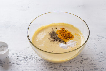 Bowl of chickpea dough with spices: black pepper, turmeric, salt, soda. Cooking vegan chickpea omelet on light gray textured backdrop