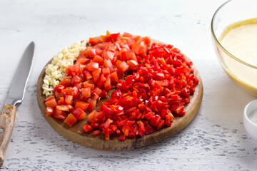 Wooden board with chopped vegetables: red bell pepper, tomatoes, garlic. Cooking vegan chickpea omelet on light gray textured background