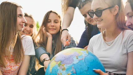 A group of cheerful girls is exploring the globe of the world in the meadow.