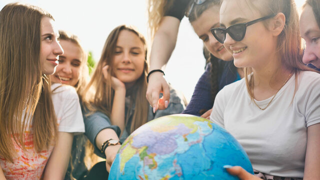 A group of cheerful girls is exploring the globe of the world in the meadow.