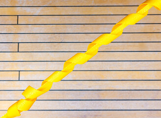 A yellow cargo strap stretched against the backdrop of a teak deck.