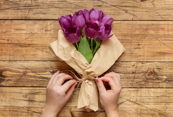 Hands wrapping purple tulips bouquet in paper over wooden table