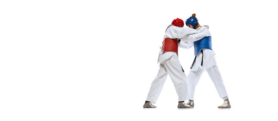 Portrait of two young women, taekwondo athletes practicing, fighting isolated over white background. Concept of sport, skills