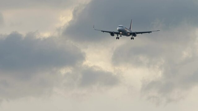 Passenger jet plane descending for landing in cloudy sky, long shot. Tourism and travel concept.