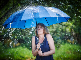 Outdoor portrait of young beautiful happy young woman holding blue umbrella, posing under rain in the summer rain