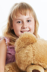 A portrait of a little blonde girl smiling and hugging her teddy bear. Isolated on white background.