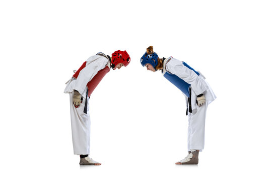 Studio shot of two young women, taekwondo athletes greeting each other isolated over dark background. Concept of sport, skills