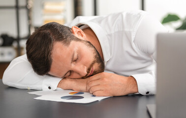 Tired businessman sleeping at his desk after a long analysis of a sales report, chronic sleep lack