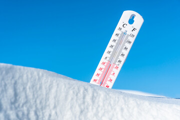 The thermometer lies on the snow and shows a negative temperature in cold weather on the blue...
