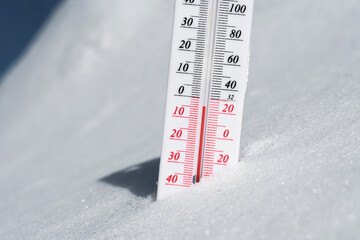 The thermometer lies on the snow and shows a negative temperature in cold weather on the blue sky.Meteorological conditions with low air and ambient temperatures.Climate change and global warming