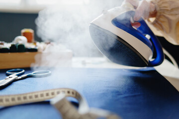 Woman ironing fabric on iron board with steaming iron.